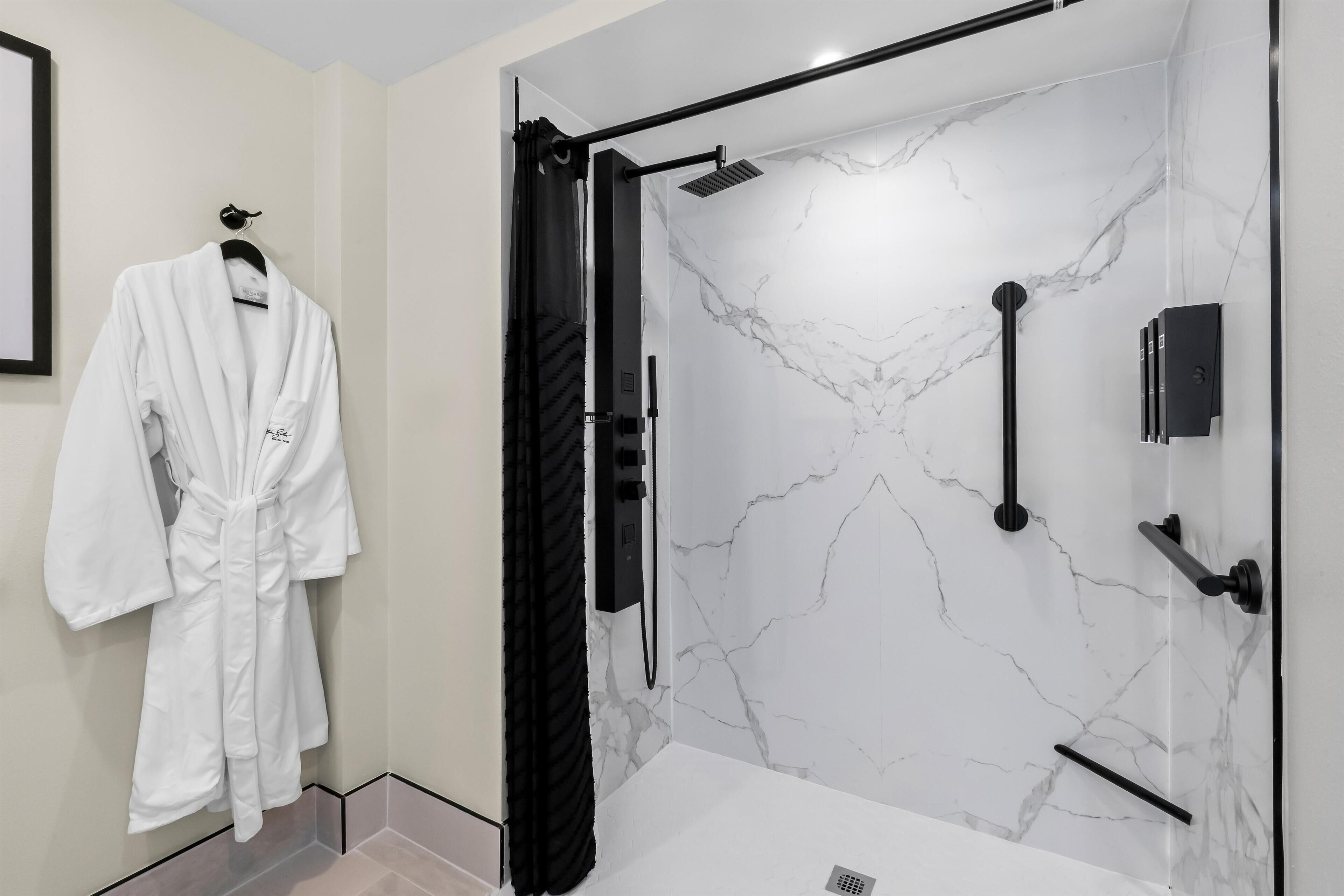 A modern bathroom with a marble wall, a black shower curtain, and a white robe hanging on the wall.