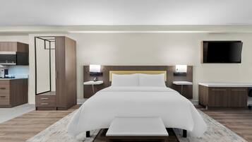 A modern hotel room with a large bed, bedside tables, a flat-screen TV, and a kitchenette.