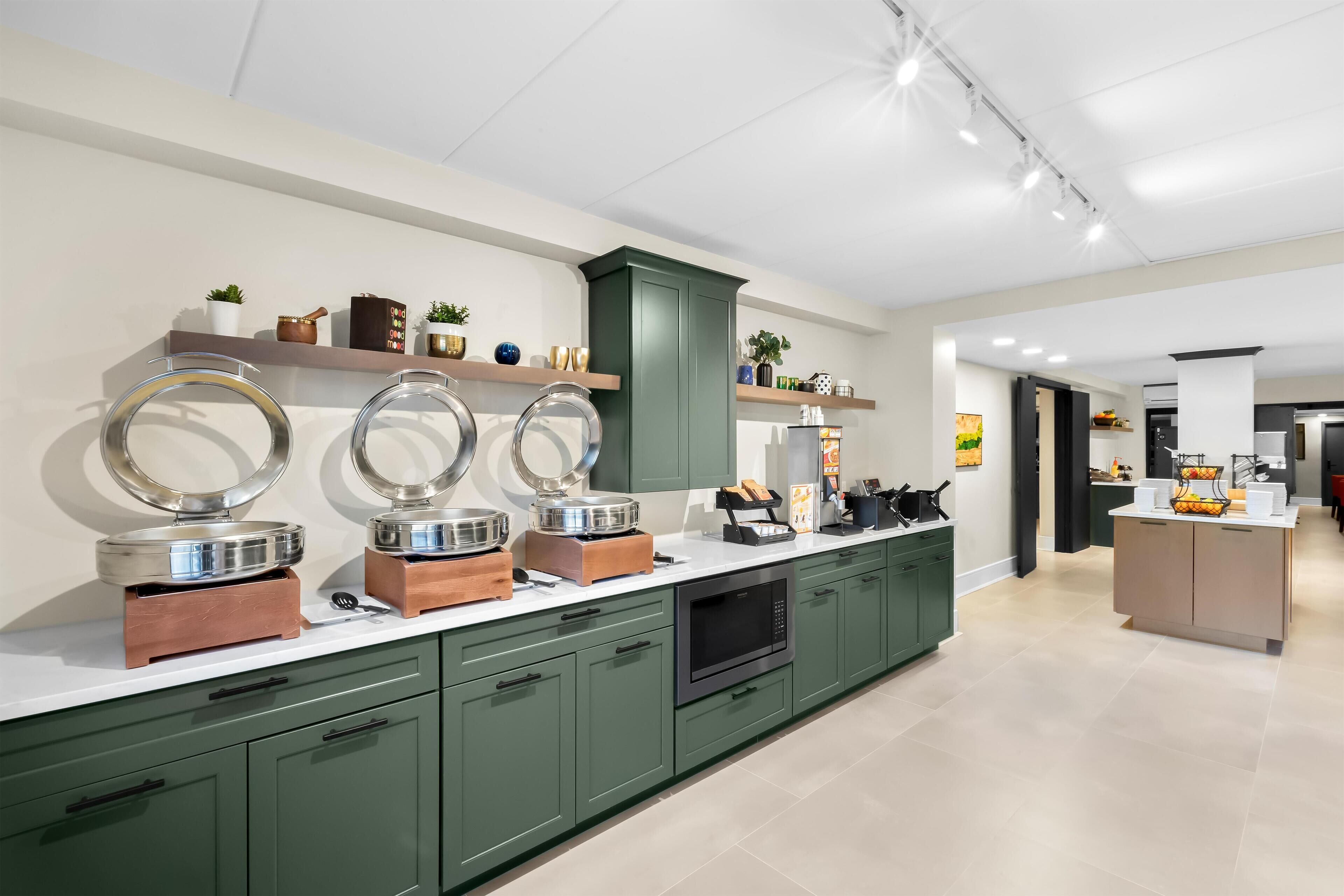 Una cocina moderna con gabinetes verdes, encimera blanca y horno empotrado.