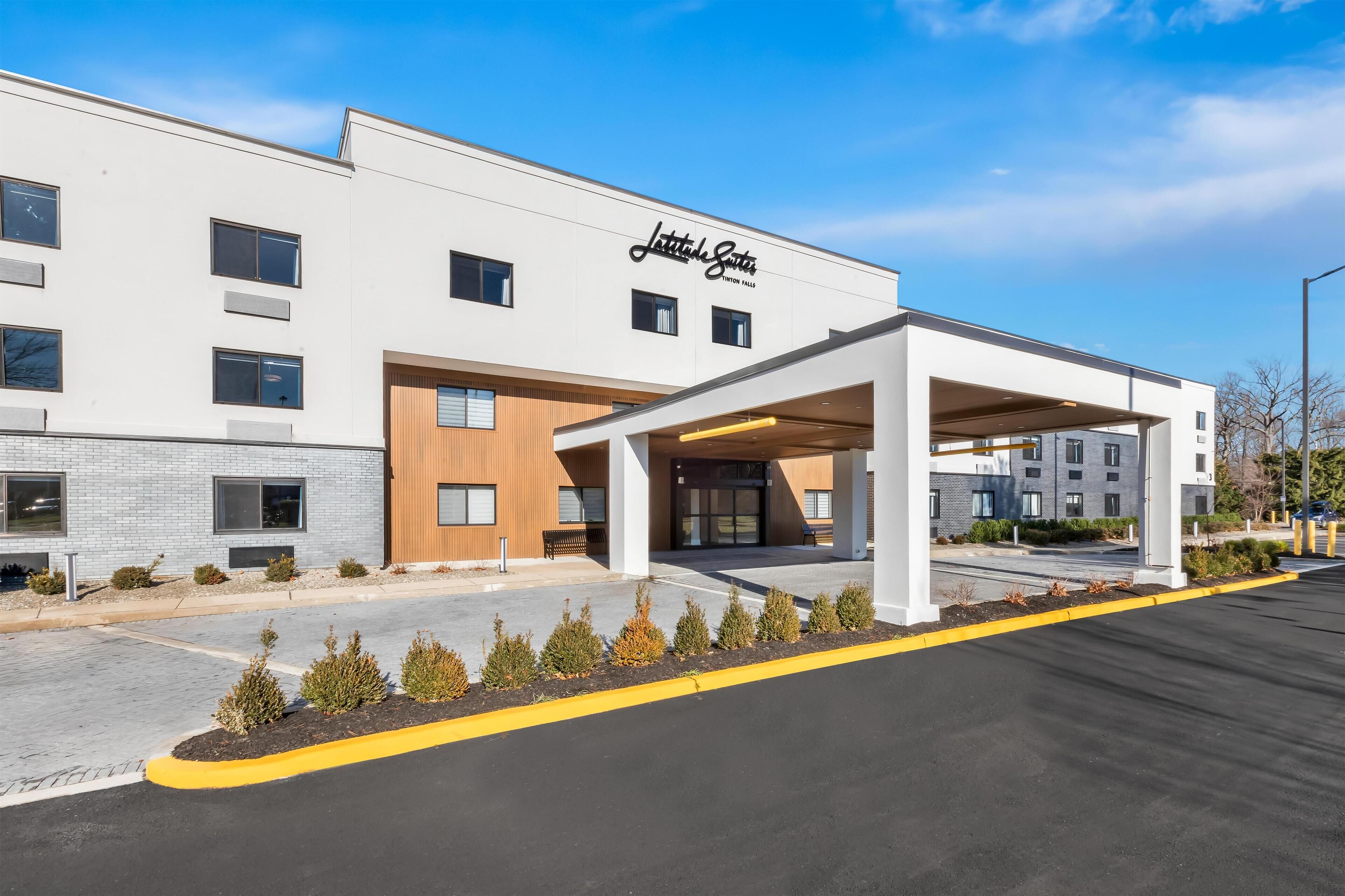A modern hotel with a white facade, a covered entrance, and a parking lot.