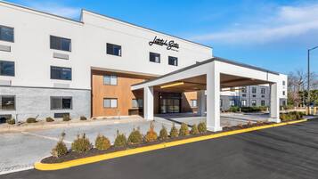 A modern hotel with a white facade, a covered entrance, and a parking lot.