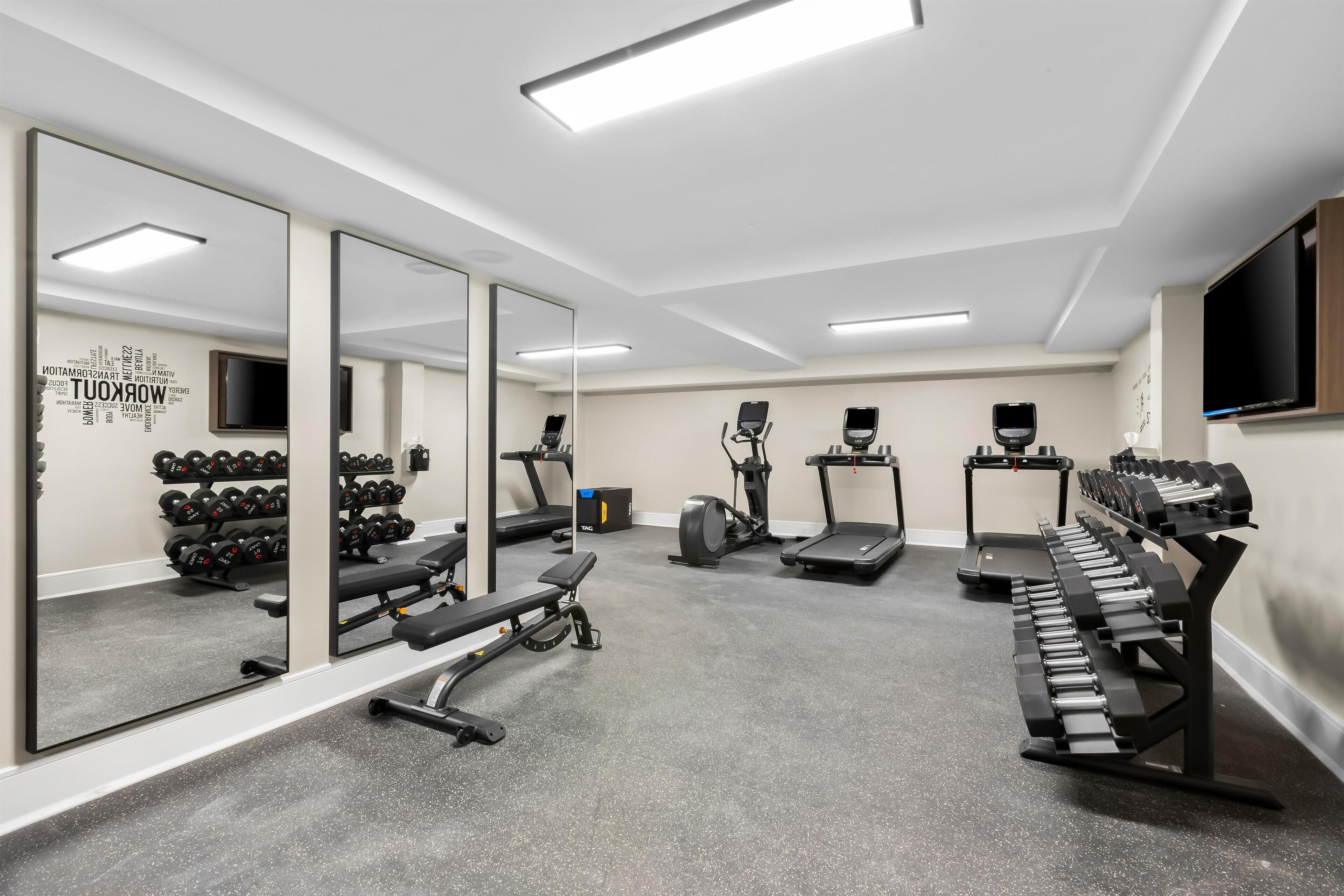 A modern gym with cardio machines, weightlifting equipment, and a large mirror.
