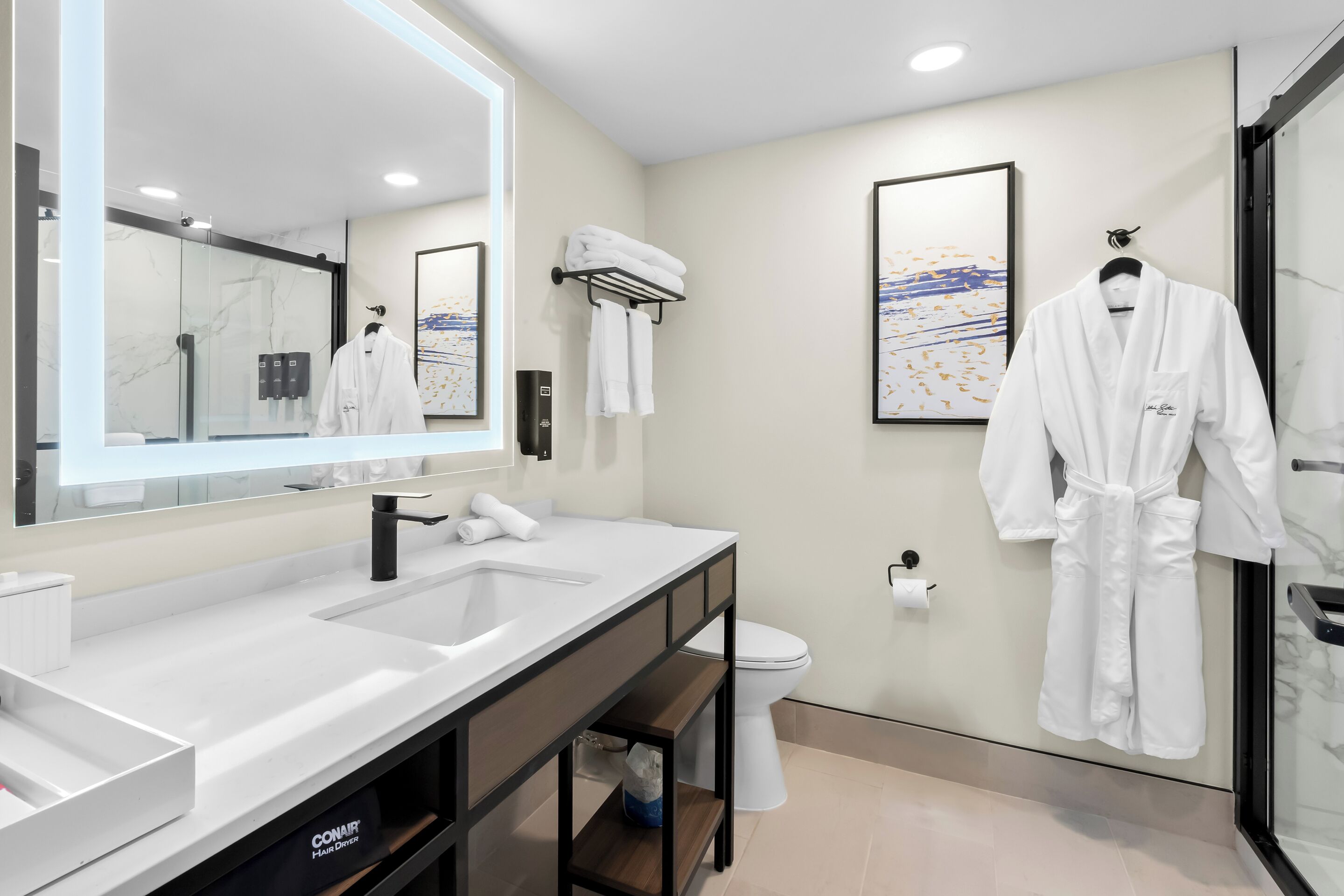Un baño moderno con un espejo grande, lavamanos dobles, inodoro y cabina de ducha con mampara de vidrio.