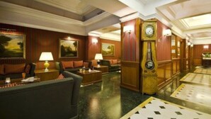A lobby with a grand piano, plush seating, and a clock on the wall. - Hotel Morgana (Rome)