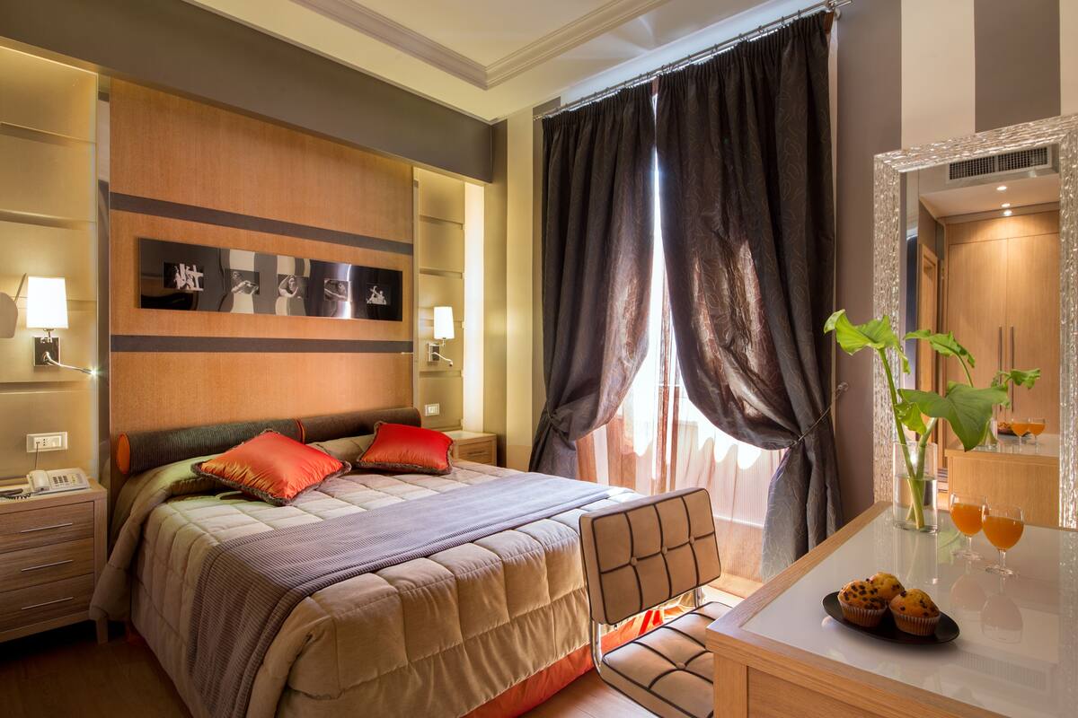 A hotel room with a bed, bedside table, lamp, and a mirror.