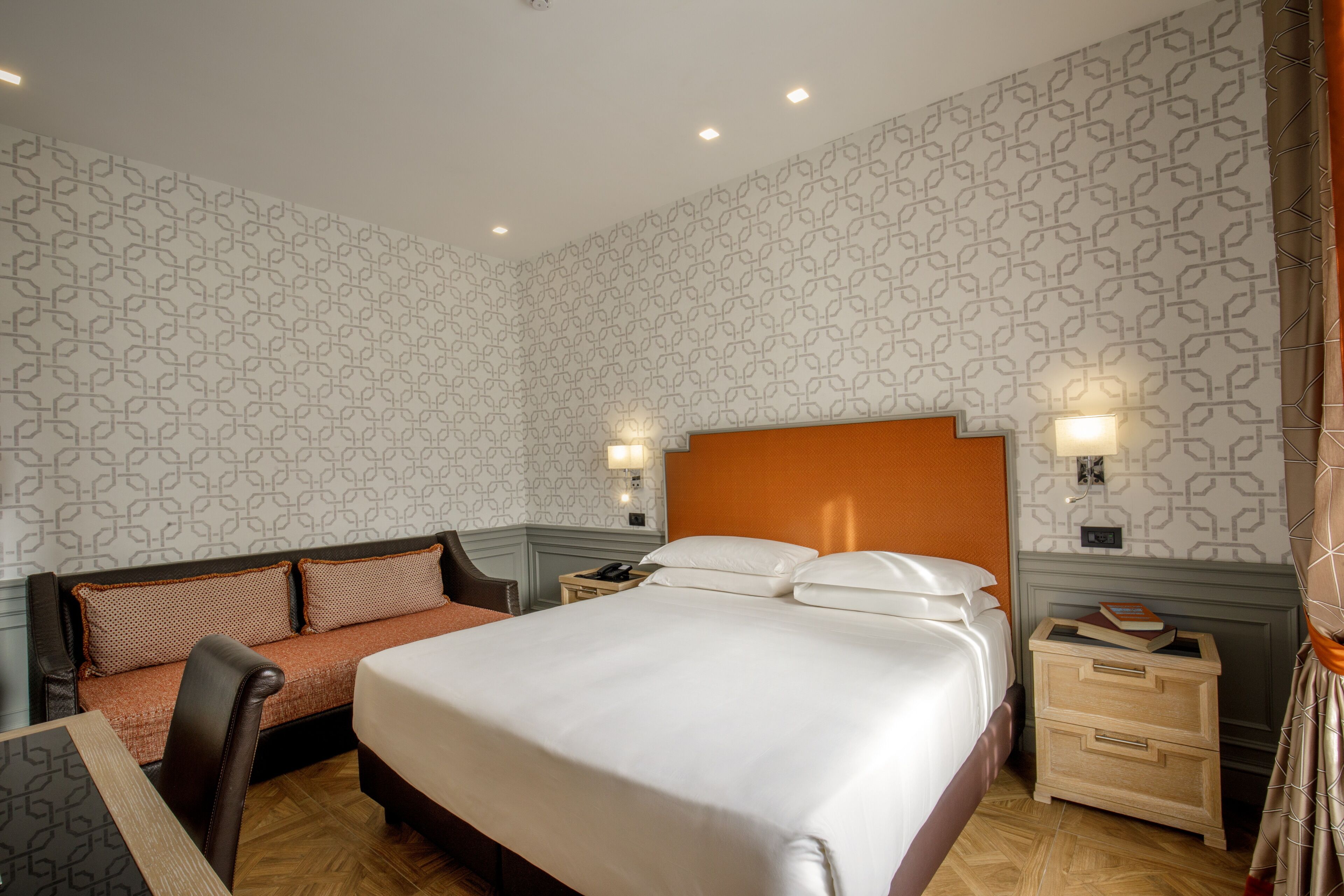 Une chambre d’hôtel avec un grand lit, un canapé, une table de chevet et un mur orné d’un motif géométrique.