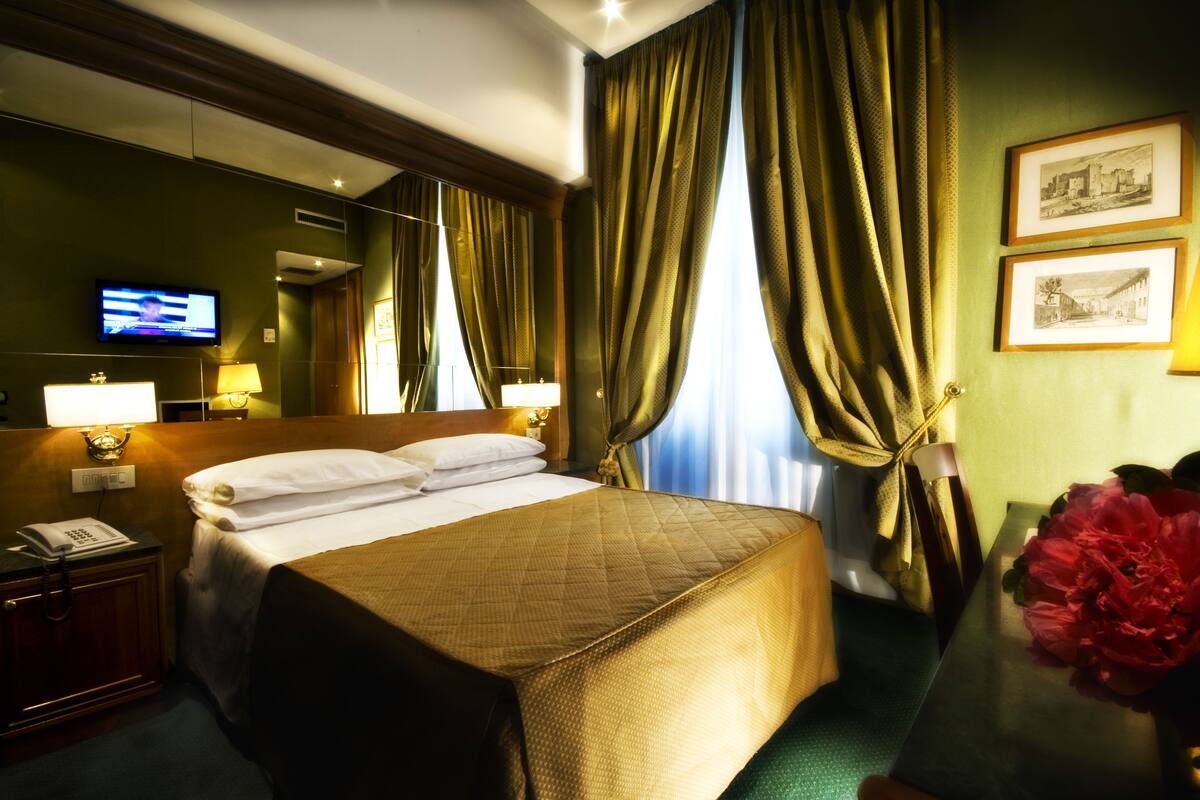 A hotel room with a bed, bedside lamps, a television, and a telephone on a nightstand.