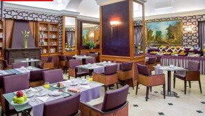 A restaurant with multiple tables and chairs, a bookshelf, and a painting on the wall. - Hotel Morgana (Rome)