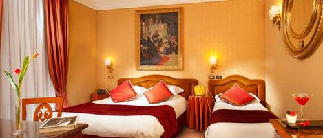 A hotel room with two beds, a painting on the wall, a mirror, and a desk with a vase of flowers.