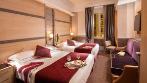 A hotel room with two beds, a sofa, a TV, and a small table with a tray of food and glasses. - Hotel Morgana (Rome)