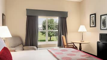 A hotel room with a bed, a chair, a table, a TV, and a window with curtains.