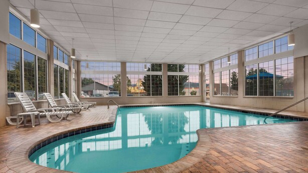 An indoor swimming pool with clear views through large windows, a wooden deck, and lounge chairs.