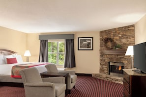 A hotel room with a bed, a desk, a fireplace, and a television. - Ramada by Wyndham Pigeon Forge North (Pigeon Forge)