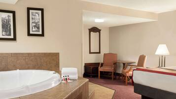 Habitación de hotel con una bañera grande, una cama, una silla, una mesa y un espejo.