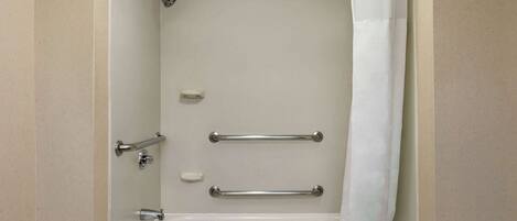 A bathroom with a bathtub, grab bars, a showerhead, and a towel rack.