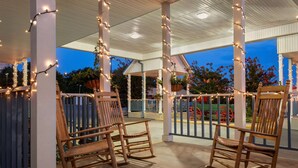 A covered outdoor area with wooden rocking chairs and string lights.