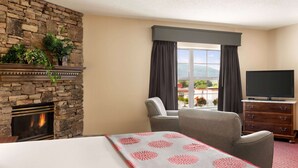 A hotel room with a stone fireplace, a large bed, a television, and a view of the outdoors.