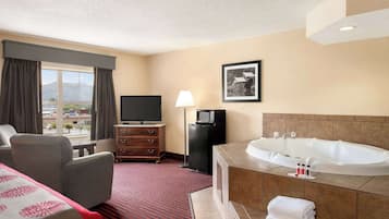 Habitación de hotel con una cama grande, un sofá, un televisor, un pequeño televisor, una bañera y una ventana con cortinas.