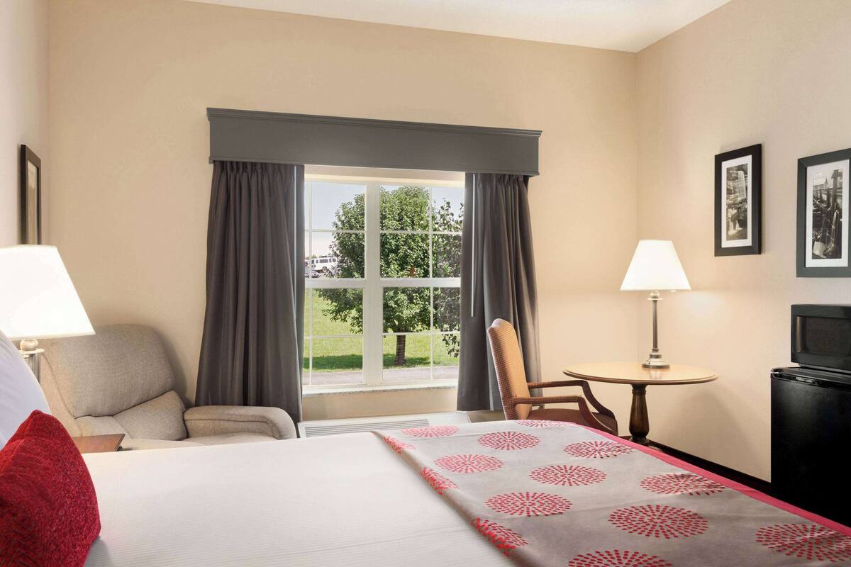 Habitación de hotel con cama, silla, mesita, televisor y ventana con cortinas.