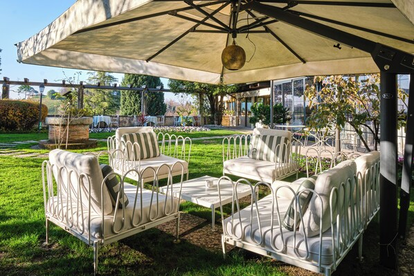 A covered outdoor seating area with white metal furniture and a large umbrella.