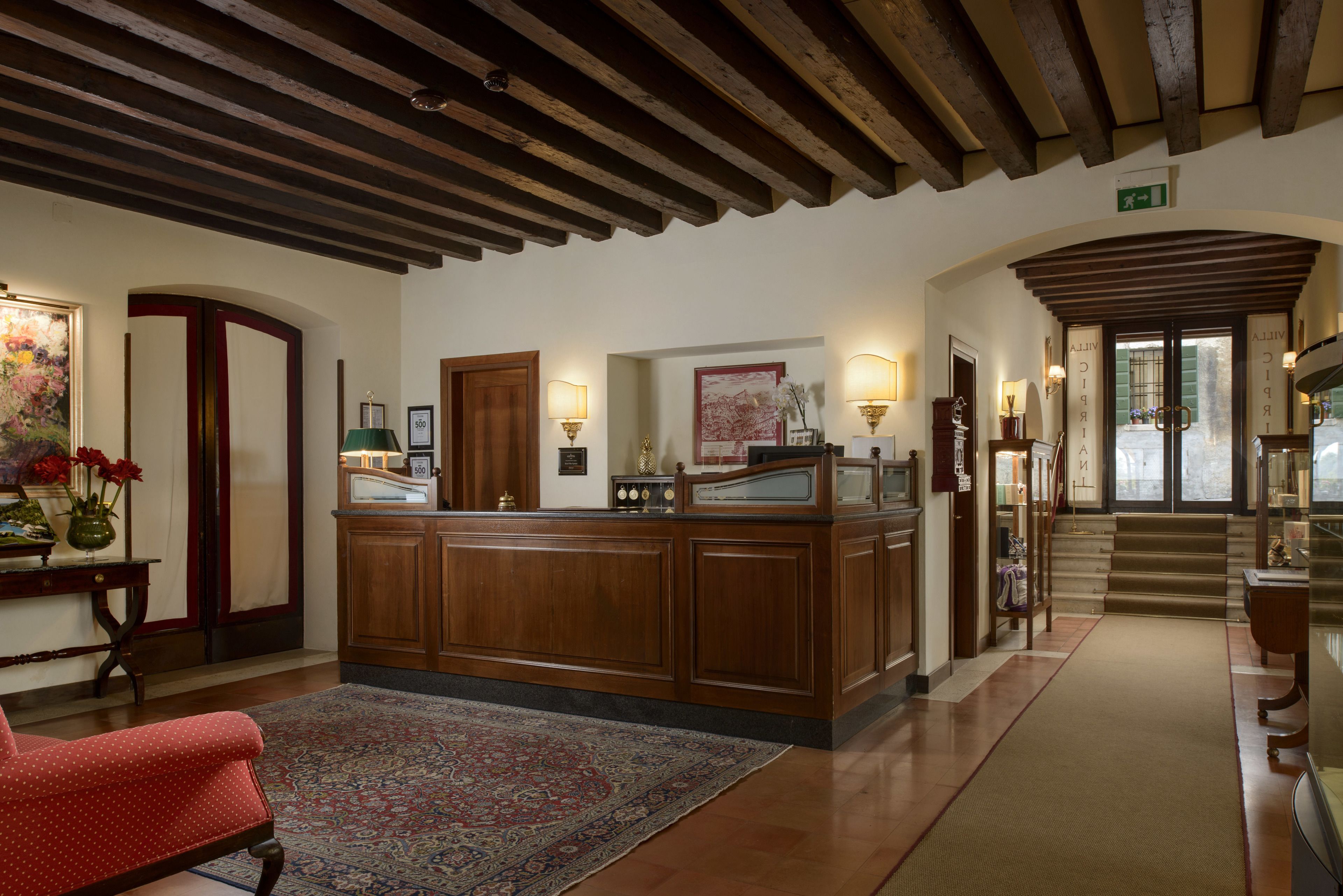 A reception area with a wooden reception desk, a red upholstered chair, and a patterned rug.