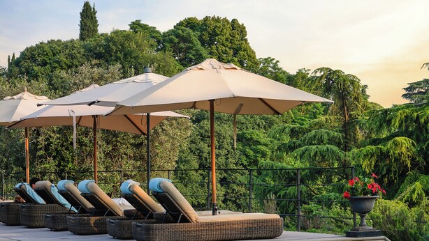 Zona de piscina con sillones de descanso y sombrillas, rodeada de abundante vegetación.