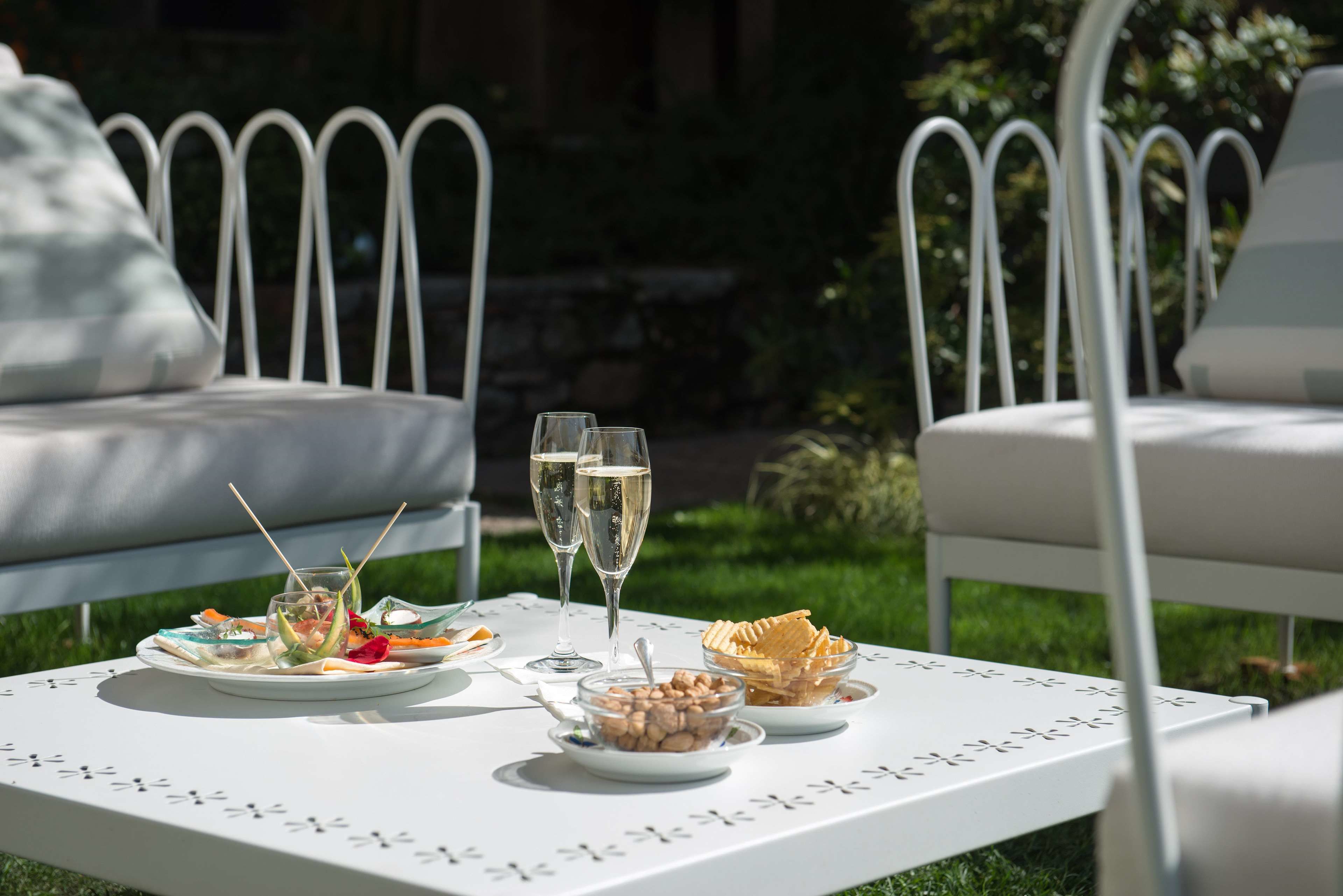 A white table with a floral pattern, set outdoors with white metal chairs.