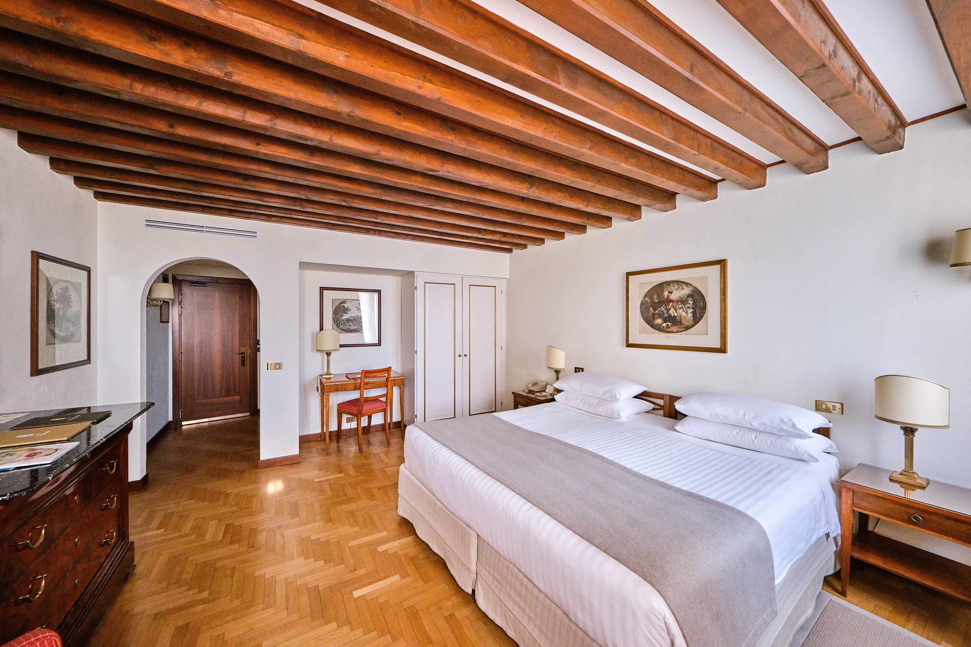 Ein Schlafzimmer mit Holzboden, einem Bett mit weißer Bettwäsche, einem Schreibtisch mit Stuhl und einem gerahmten Bild an der Wand.