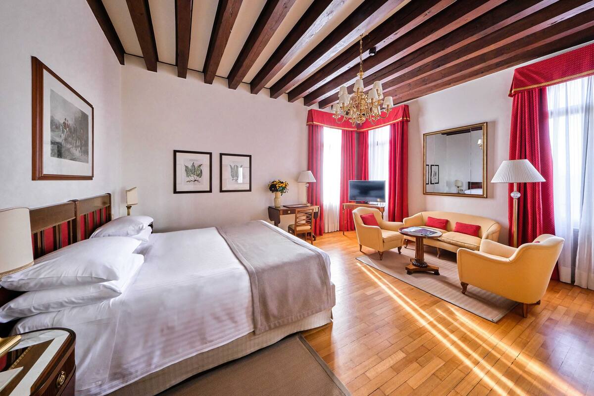 A hotel room with a large bed, a sofa, a TV, and a chandelier.