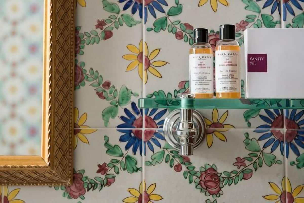 A bathroom with floral tiles, a mirror, a glass shelf with toiletries, and a vanity unit.