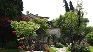 Un jardín con una fuente de piedra circular, un camino de piedra y un edificio al fondo.