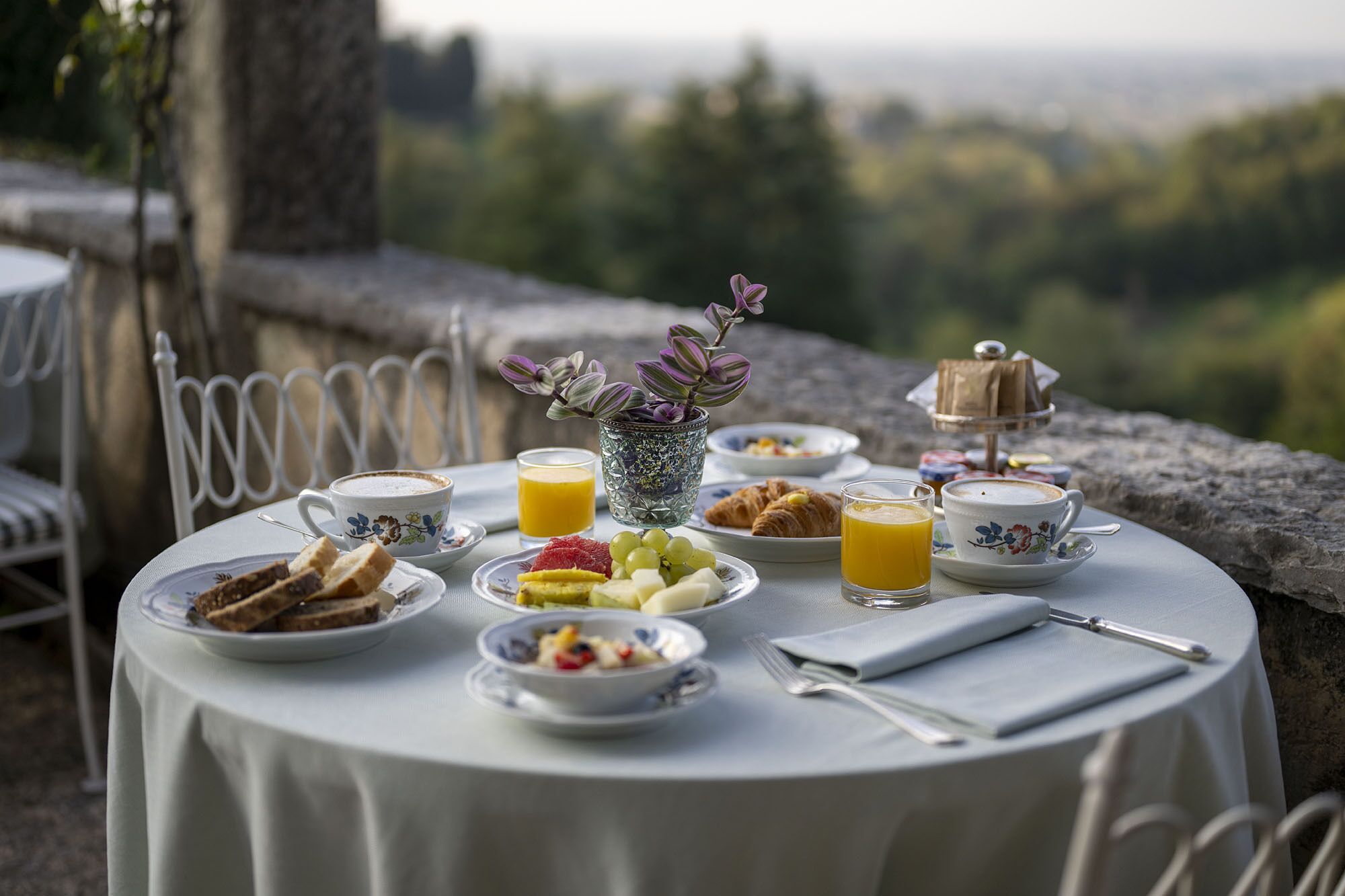 Ein Frühstückstisch mit Croissants, Früchten und Kaffee, mit Blick auf eine malerische Landschaft.