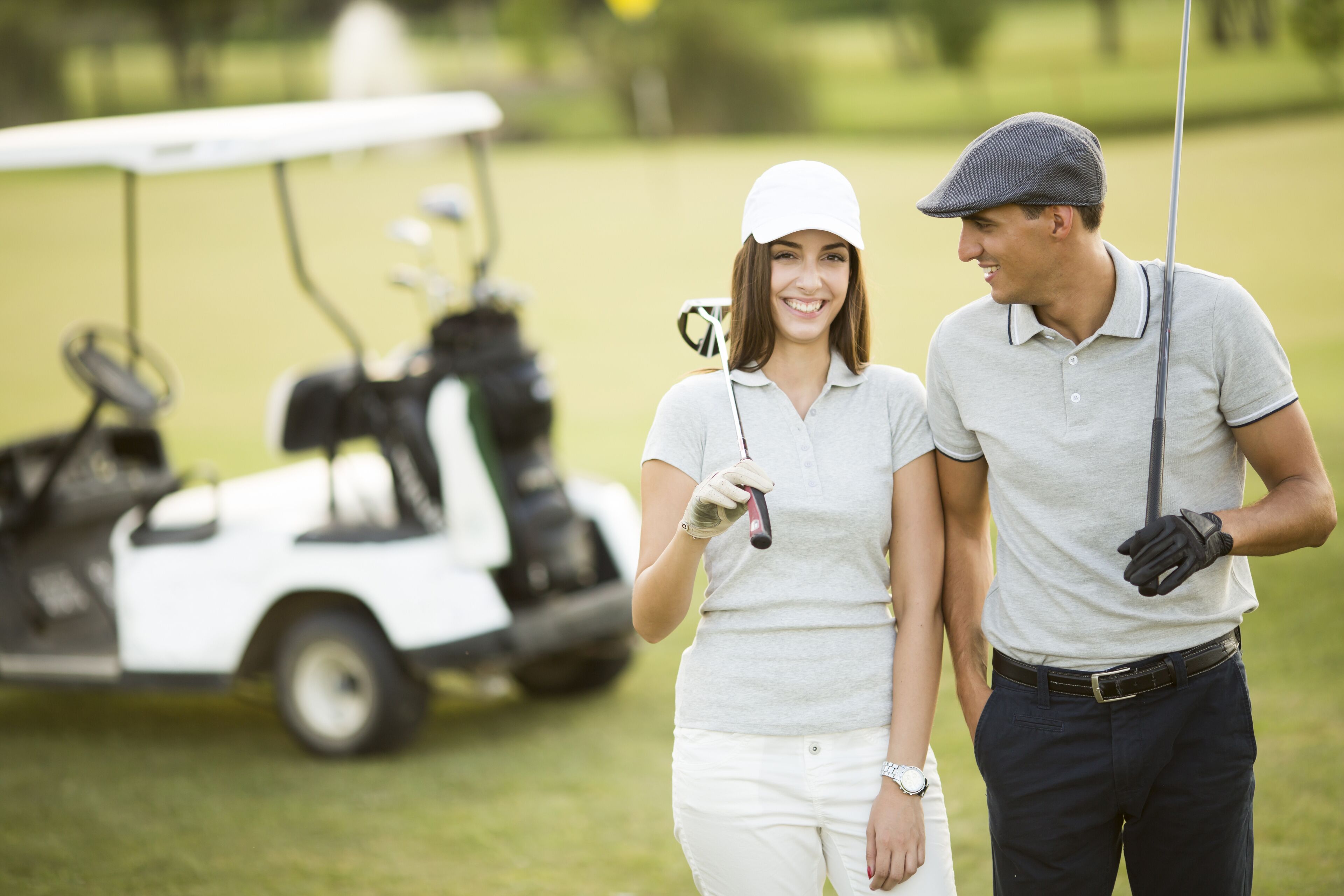 Een golfkarretje en twee personen op een golfbaan.
