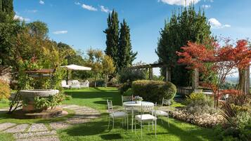Un jardin avec une table ronde et des chaises, entouré de verdure et bordé d’un chemin de pierres.