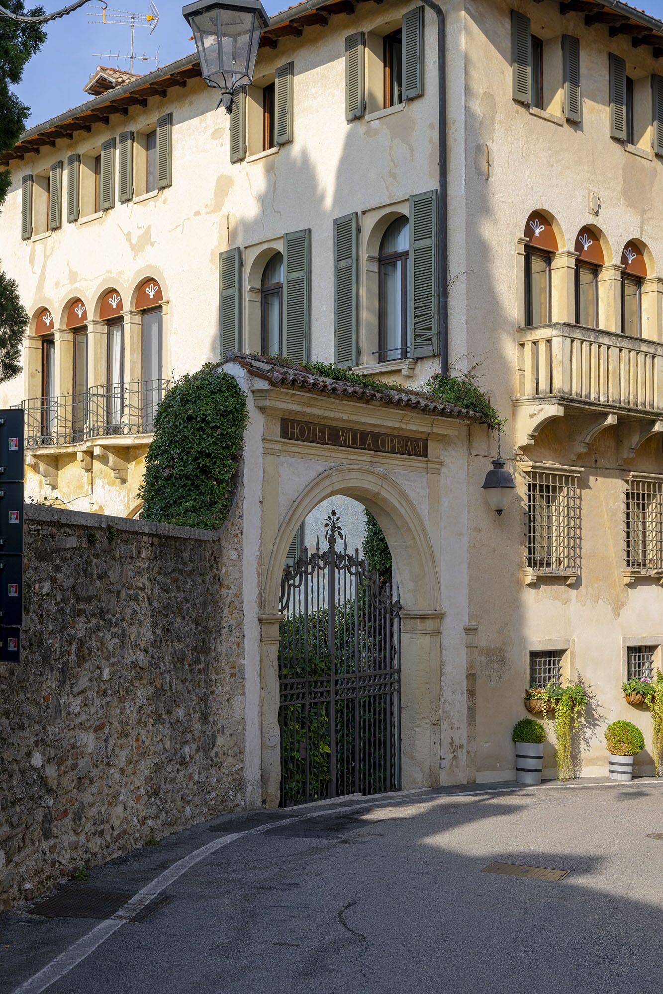A historic building with a stone wall, an arched entrance, and a sign reading "Hotel Villa Cipriani".