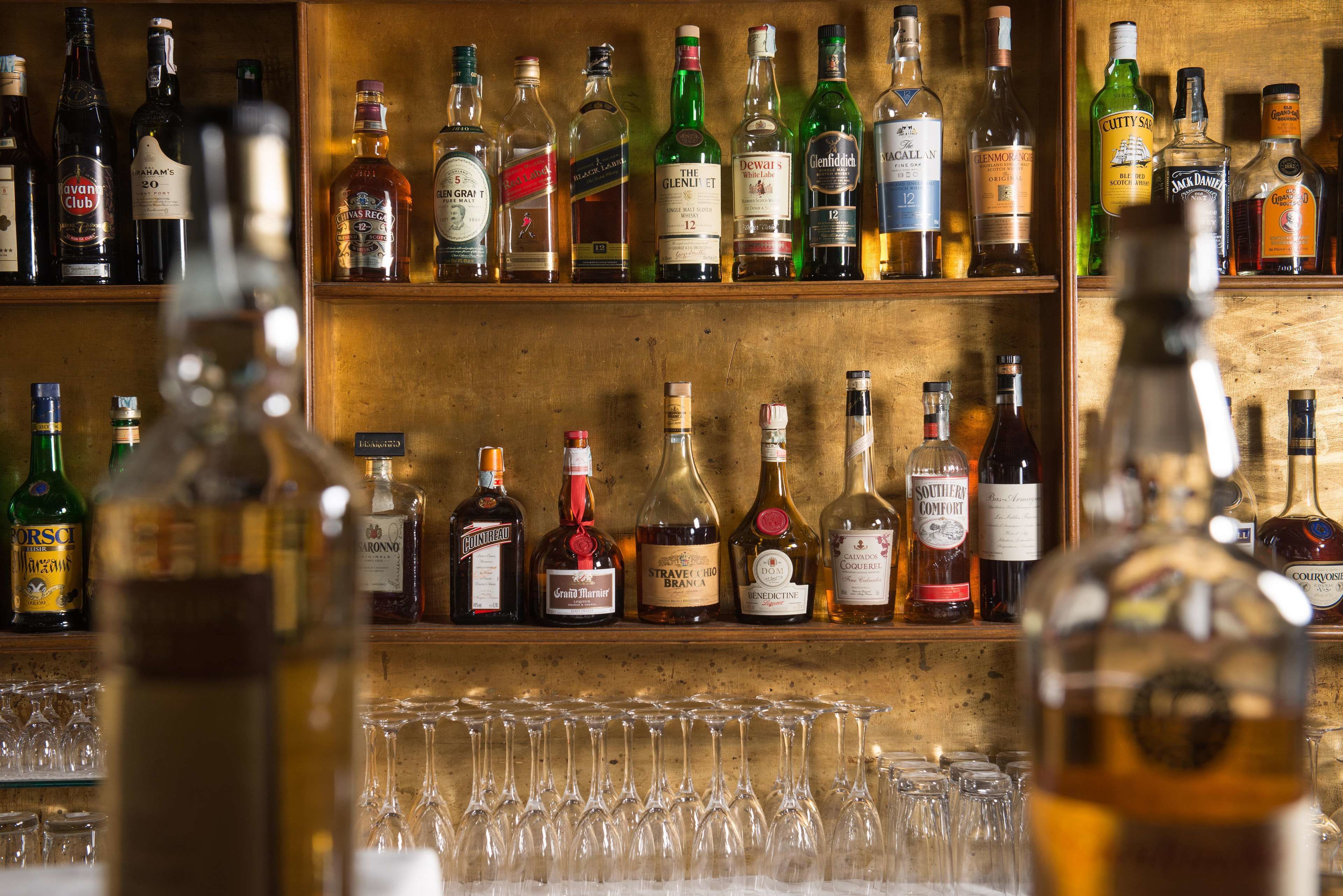 Eine Bar mit Regalen voller Spirituosenflaschen und einer Auswahl leerer Gläser.