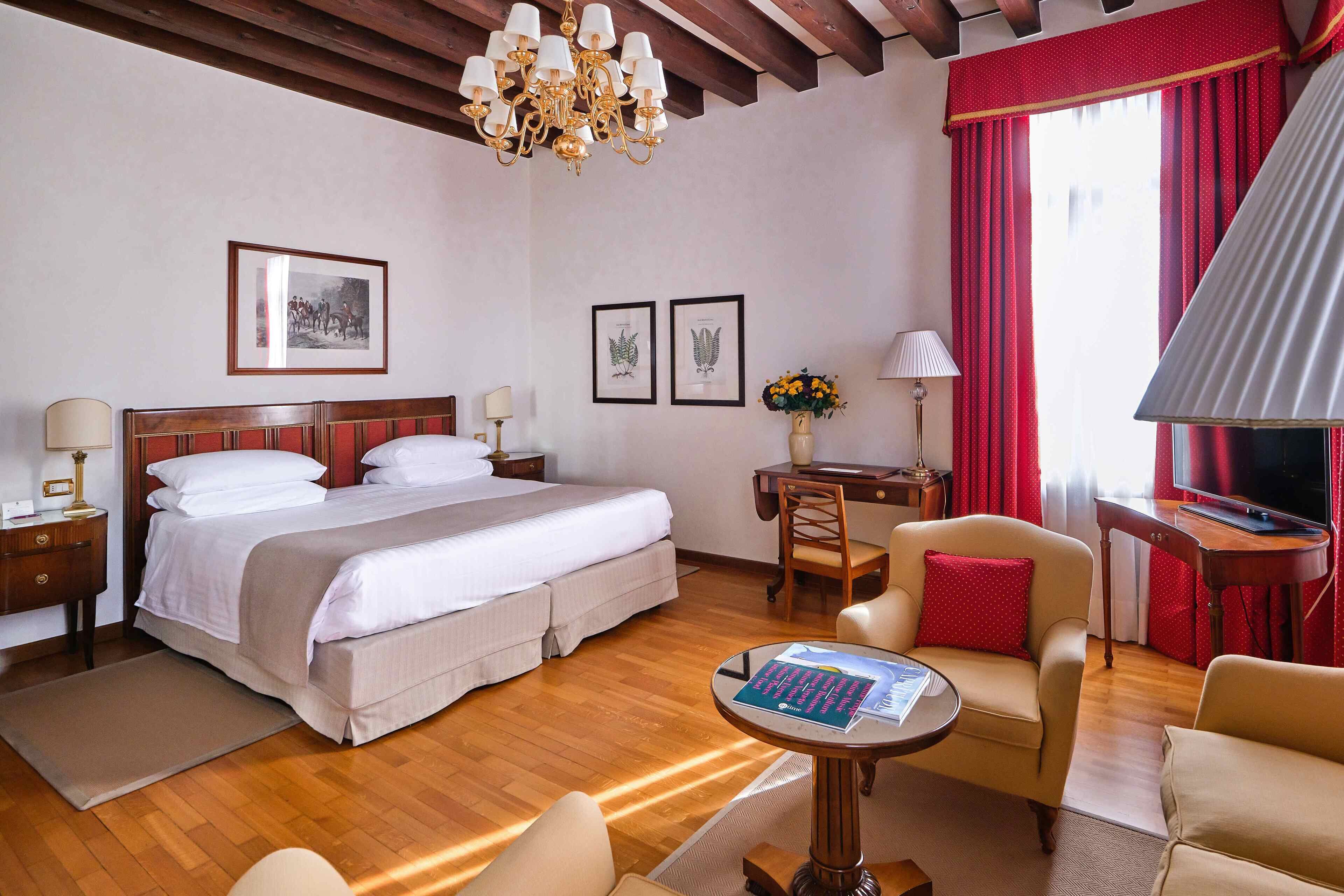 Habitación de hotel con una cama grande, un escritorio, dos sillas, un televisor y una araña.