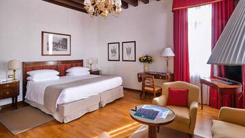 Habitación de hotel con una cama grande, un escritorio, dos sillas, un televisor y una araña.
