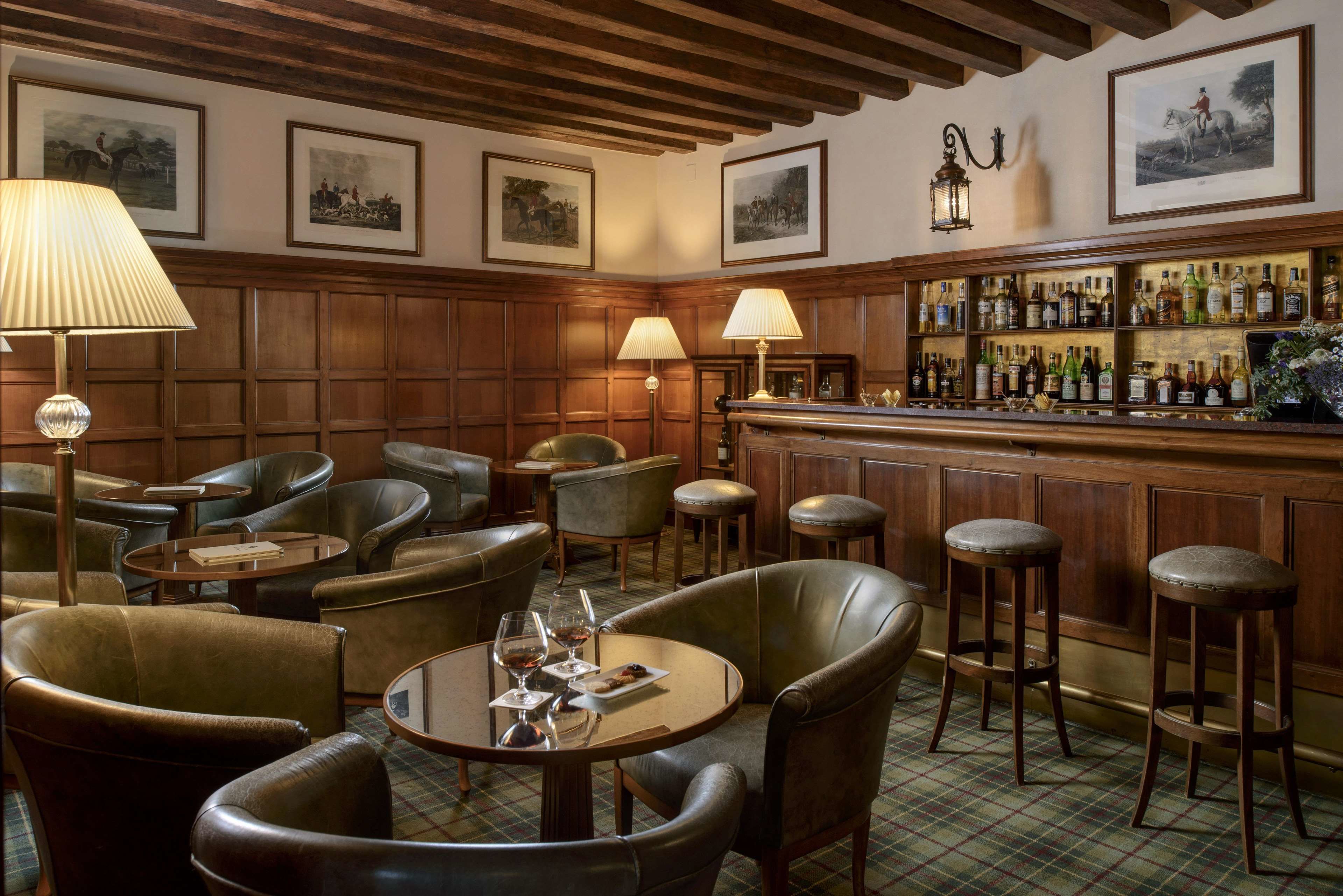 Un coin bar avec des fauteuils en cuir, une table ronde avec des verres et un bar bien garni de bouteilles.