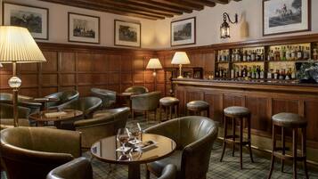 Un coin bar avec des fauteuils en cuir, une table ronde avec des verres et un bar bien garni de bouteilles.