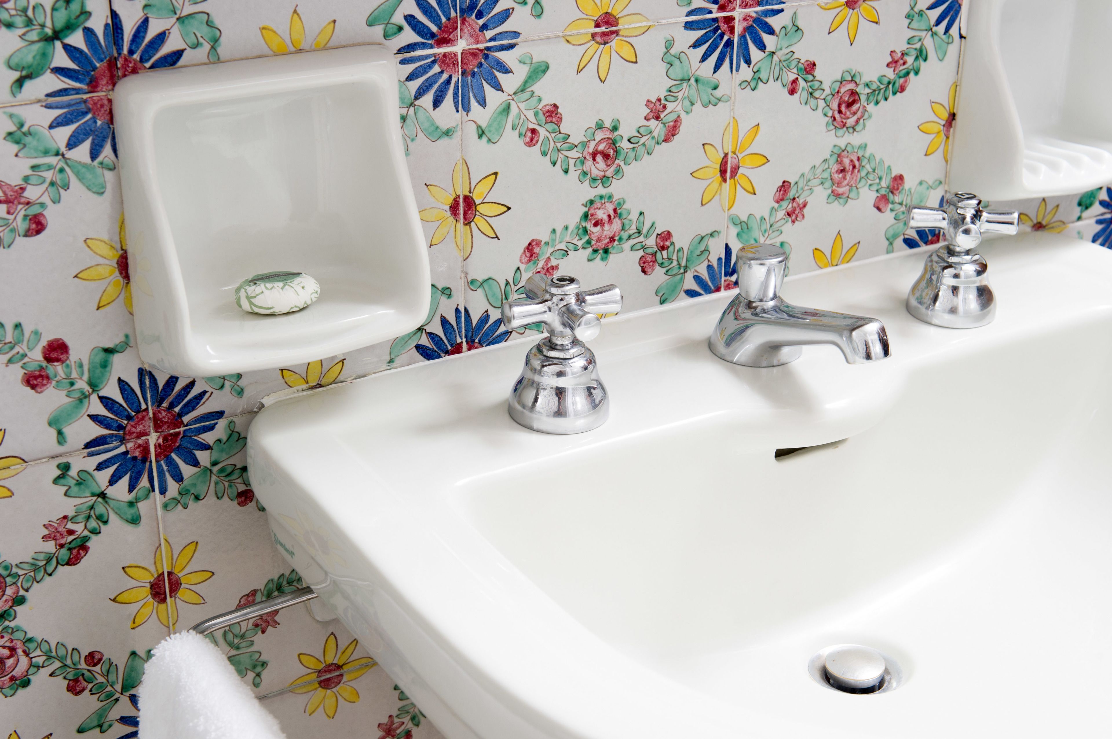 A bathroom with a white sink, two faucets, a mirror, and a floral-patterned tile backsplash.