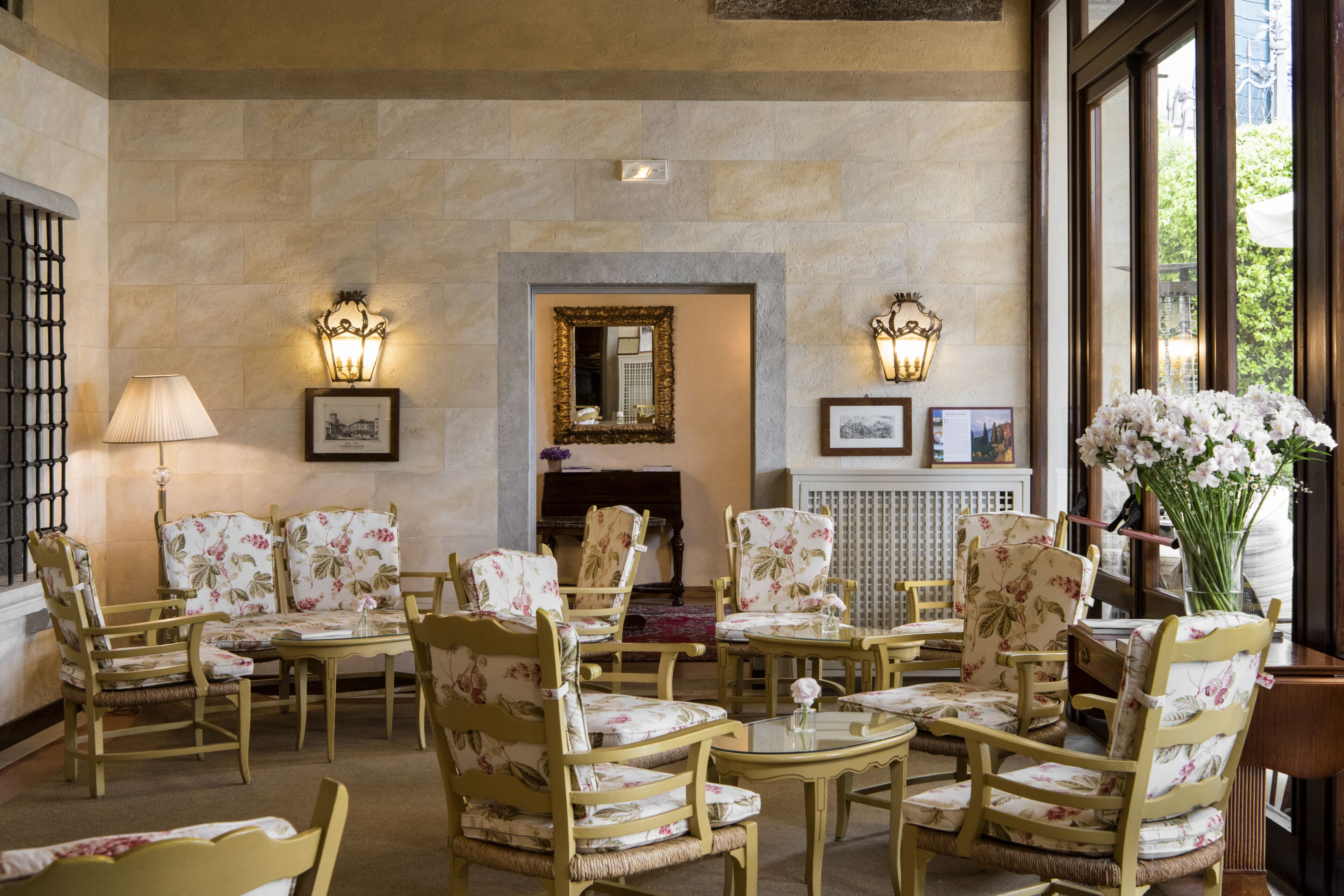 A room with a fireplace, floral-patterned chairs, and tables.