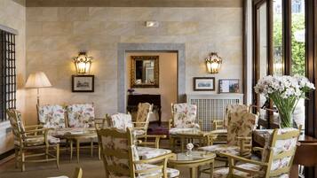 A room with a fireplace, floral-patterned chairs, and tables.