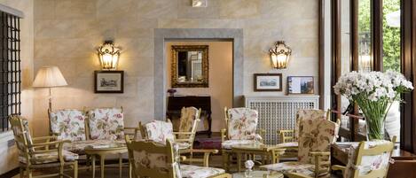 A room with a fireplace, floral-patterned chairs, and tables.