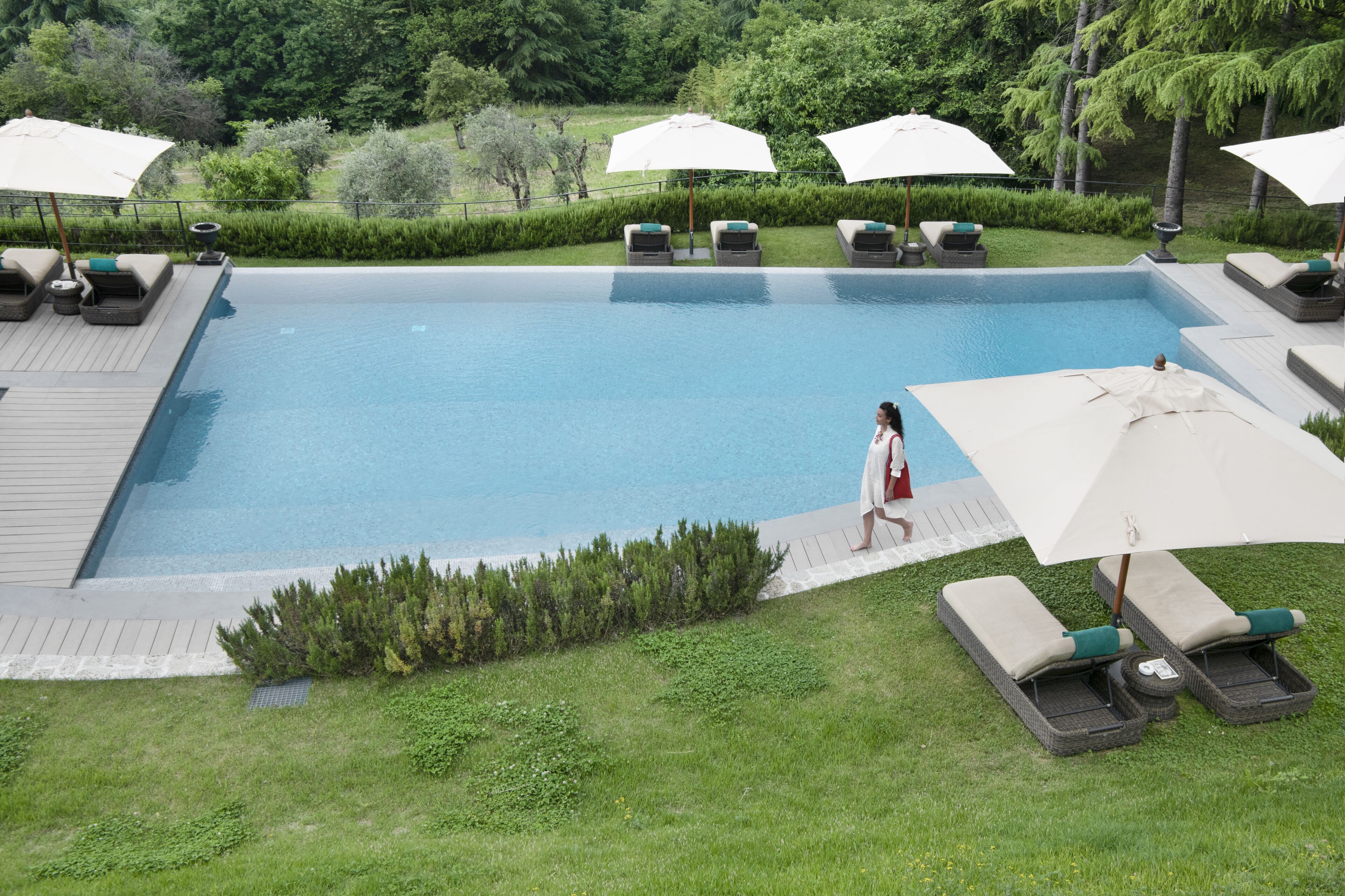 Piscina com espreguiçadeiras e guarda-sóis, rodeada por vegetação.