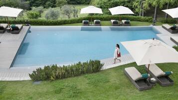 Piscina com espreguiçadeiras e guarda-sóis, rodeada por vegetação.
