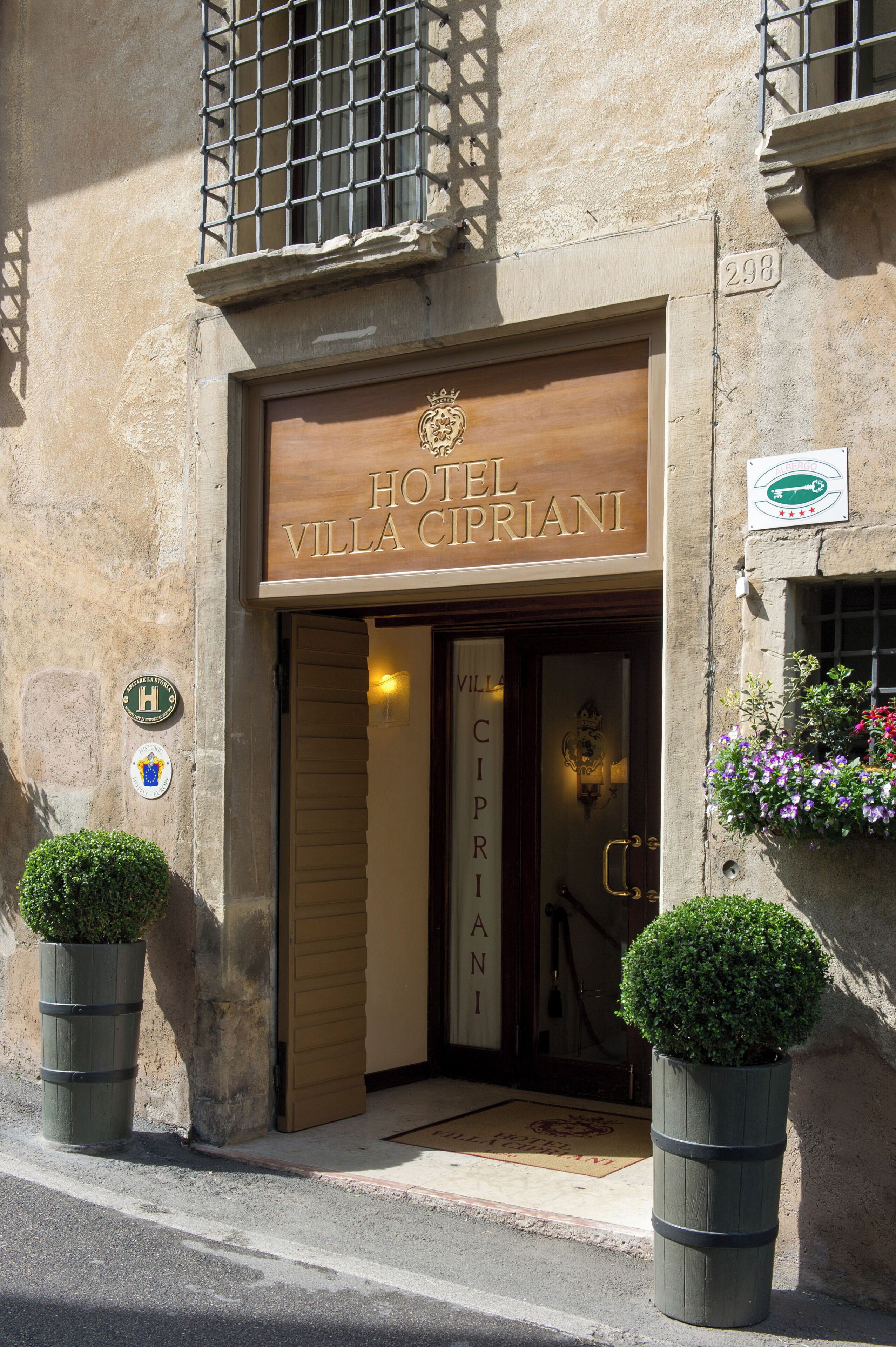 El exterior del Hotel Villa Cipriani, con fachada de madera, un cartel con el nombre del hotel y dos plantas en macetas en la entrada.