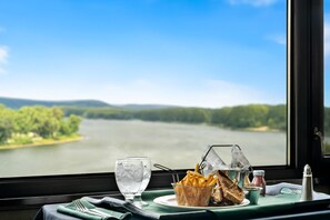 Una mesa de comedor con vistas a un lago, una cesta de papas fritas, un sándwich y un vaso de agua.