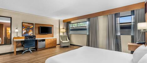 A hotel room with a large bed, a desk with a computer, a chair, a TV, and a window with curtains.