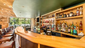 Una zona de bar con un mostrador de madera curvo, asientos y estantes llenos de botellas de licores.